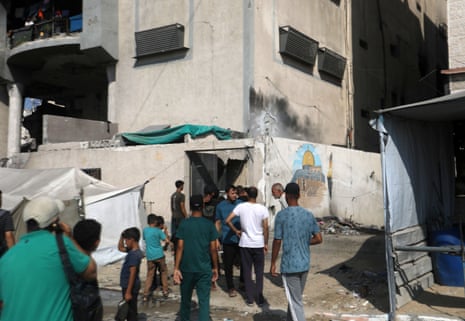 About a dozen Palestinians gather outside a building hit by an Israeli airstrike.