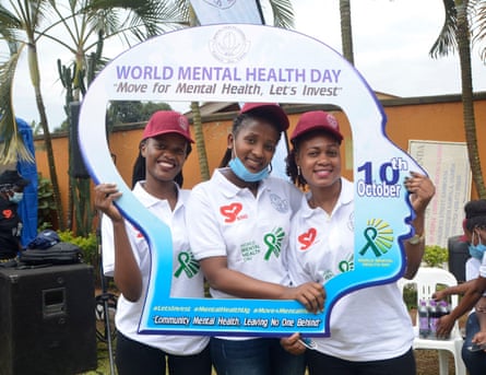 Three women stand inside a cutout of a head in profile which is covered in World Mental Health Day logos