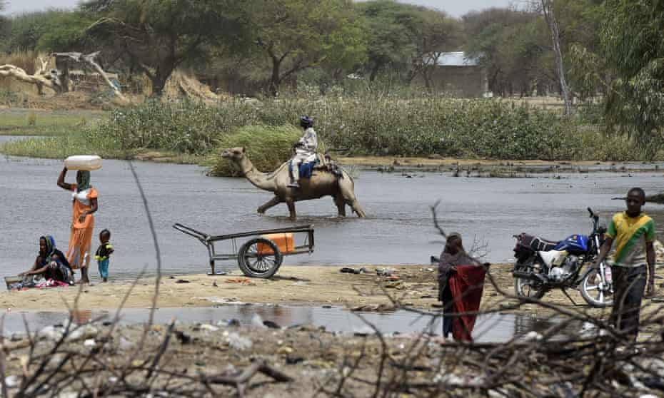 People washing clothes and a man riding a camel in shallow waters of Lake Chad on 6 April 2015 in N’Gouboua.