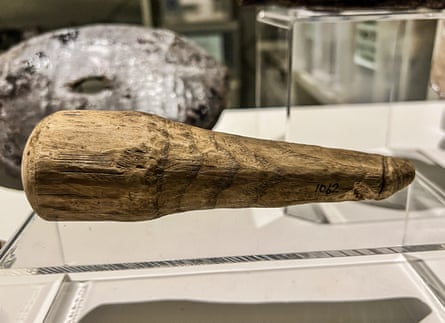 An antiquarian phallus made of wood, with a pointed end, on a see-through stand in a museum.