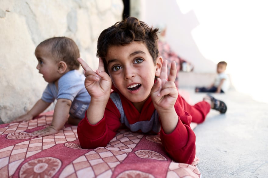 A small boy makes a ‘v for victory’ gesture as he lies next to a baby 