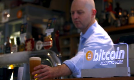 publican places a beer on the counter of a pub in Sydney Australia next to a sign that says "bitcoin accepted here"