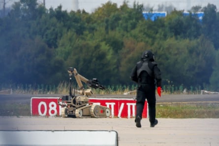 A police officer in protective clothing walks next to an explosive-disarming robot