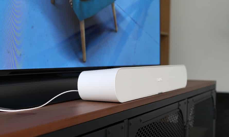 The Sonos Ray soundbar viewed from an angle sitting on a TV cabinet in front of a television.