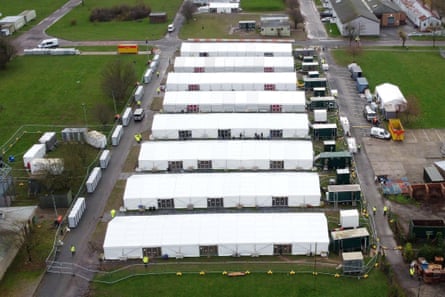 A horizontal row of eight long, white temporary buildings from above, surrounded by several green fields and roads