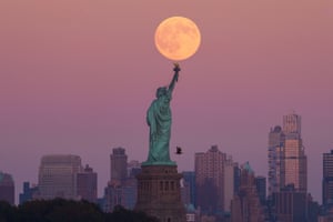 The harvest supermoon rises behind the Statue of Liberty and the Brooklyn skyline