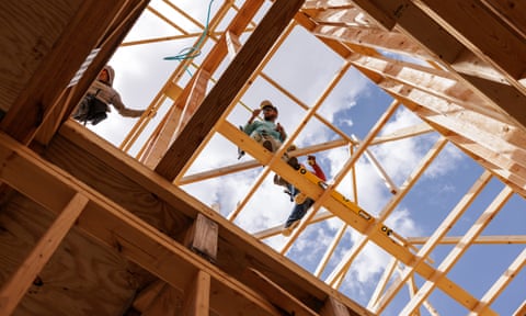 a view from the ground looking up towards constructions workers as they work on the wooden framing of what will become a townhouse