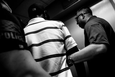 Officers hold a man in a striped shirt by his arms.