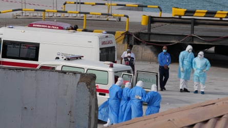 People in protective clothing walk patients, also in protective clothing, towards a waiting ambulance