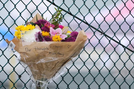 a bouquet of flowers marked with 'our thoughts + prayers' hangs on a fence