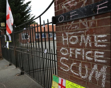Home Office Scum. An England flag has been fastened to the black iron gates. There are low-rise brick buildings in the background.