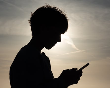 A silhouette of a child on their mobile phone