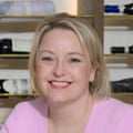 A portrait of a smiling blond woman wearing a pink cardigan