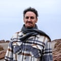 A man wearing a scarf stands on a beach.