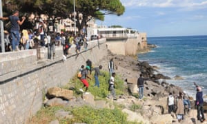 Migrants scrambling on rocks to evade border forces in Italy and enter France.