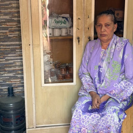 A woman dressed in a purple sari sitting next to a cupboard with a bullet hole in the glass pane and another on the frame