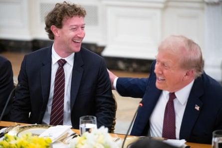 Mark Zuckerberg and Donald Trump sit at a table laughing; Trump has his hand on Zuckerberg’s back.