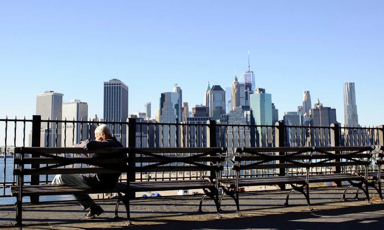 A man sits reading on a bench by the Brooklyn Heights waterfront