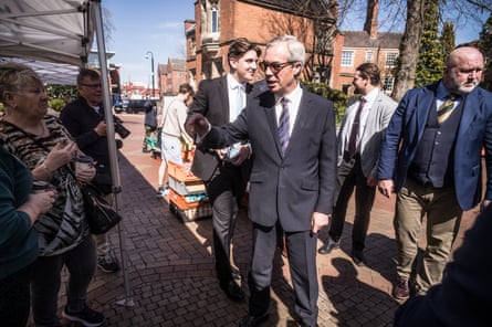 Nigel Farage, in sunglasses, chats to a woman in a market square