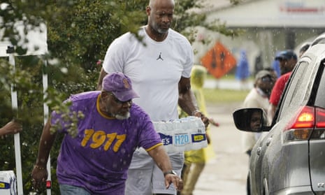 A volunteer clears a path for former NBA basketball player Erick Dampier, as he carries a case of water in the rain to a waiting car, as a coalition of social, fraternal and individuals held a water drive in south Jackson, Mississippi, this week.