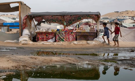 Two Palestinian children walk next to a sewage spill near tents for internally displaced people at a camp in Rafah, southern Gaza Strip.