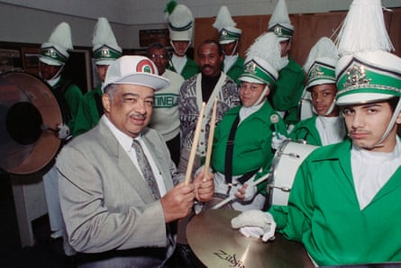 Man in suit with teenagers in green costumes with peaked hats.