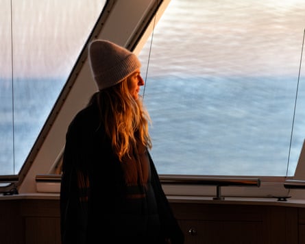A woman in a knitted hat looks out of a ship's window
