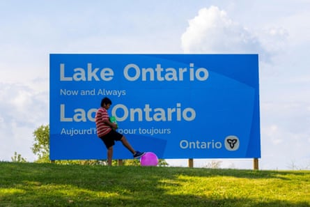 A boy plays with a ball near a sign reading “Lake Ontario, Now and Always,”