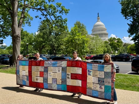 three women smile while holding a quilt that says 'PEACE'