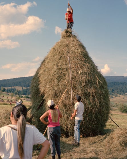 People stand at the bottom of a haystack looking up at a girl on the top adding hay