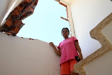 A woman stands next to a hole in a house wall