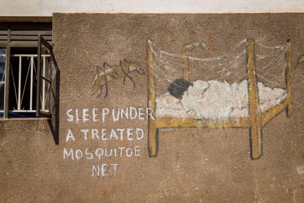 A picture on a wall of a child in a bed with a net and mosquitoes outside it, with the words ‘sleep under a treated mosquitoe net’