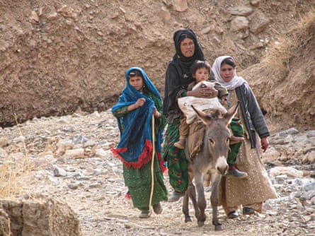 A woman rides a donkey carrying a small child while two older children walk beside