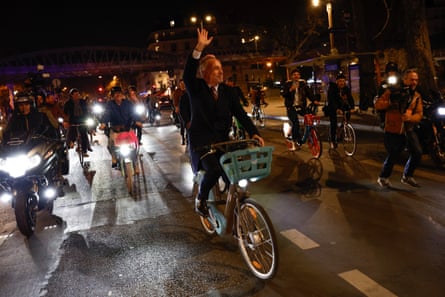 A man waving to supporters as he rides a bike in Paris at night