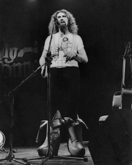 Scottish comedian Billy Connolly performing on stage in a pair of outsize, banana-shaped boots, 1977.
