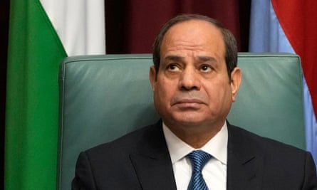 Abdel-Fatah al-Sisi, in a shirt, tie and jacket, sits in front of a flag looking up to the left, frowning