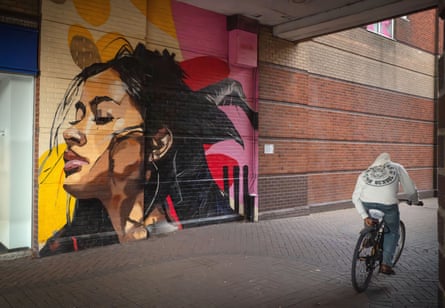 A cyclist passes a wall with graffiti showing the head of a young woman