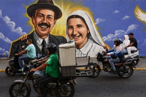 Motorcyclists ride past a mural showing the smiling faces of Blessed José Gregorio Hernández and Blessed Carmen Rendiles Martínez
