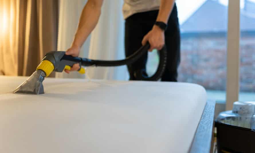 A person vacuuming a mattress.