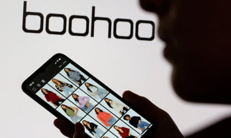 A woman in silhouette holds a smartphone displaying Boohoo clothes