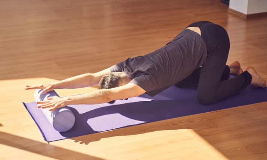 A man stretching out his arms and shoulders by placing his palms on a foam roller while in a modified child's pose