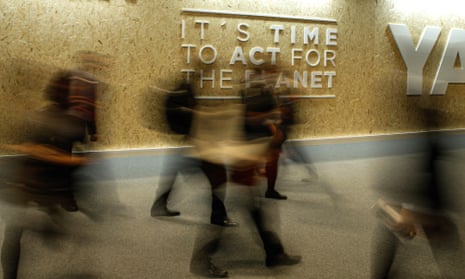 A photo of a blur of people walking quickly past a sign on the wall saying 'it's time to act for the planet'