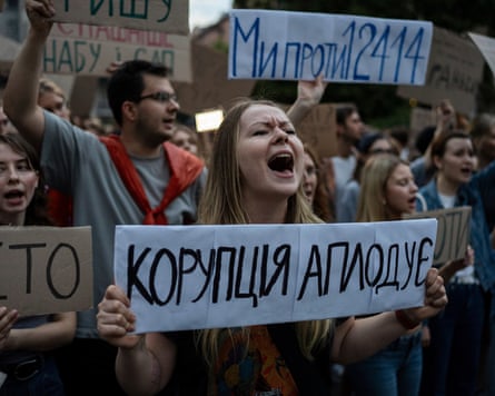 A woman chants while holding a banner that reads ‘Corruption Applauds’ in Ukrainian, while surrounded by other protesters