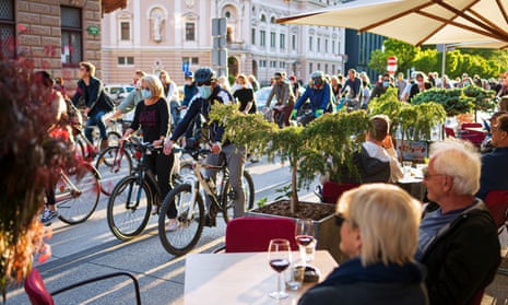 People having drinks on terraces look at Slovenian citizens, some wearing protective masks, riding their bikes as they block the centre of capital Ljubljana in protest, May 8, 2020.