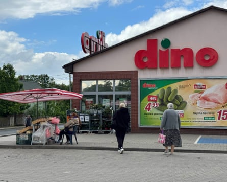 Two people walk towards a supermarket called dino. Outside there is a stall with a parasol over it.