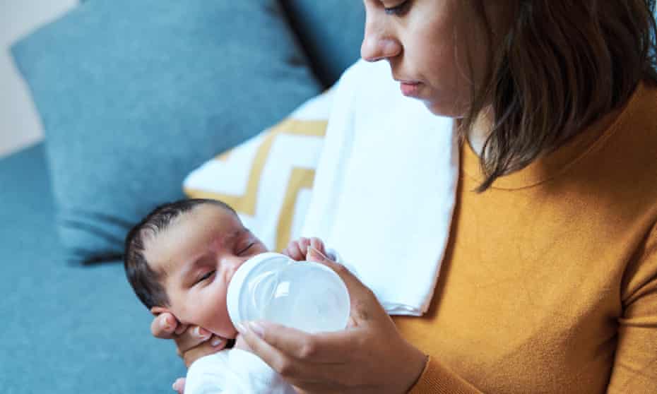 Close-up view of mother feeding her baby with infant formula bottle at home.