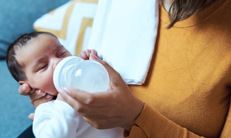 Close-up view of mother feeding her baby with infant formula bottle at home.