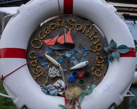 A life ring circles a round plaque with recycled plastic forming the words Clean Ocean Sailing.org and a picture of a boat on the sea