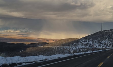 snow on hills with mountains in the distance, under a gray sky, with a road in the foreground