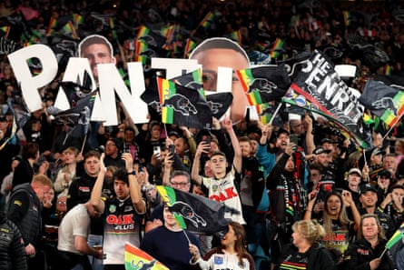 Panthers fans show their support in the stands of a football ground waving NRL team Penrith Panthers posters, flags and placards.